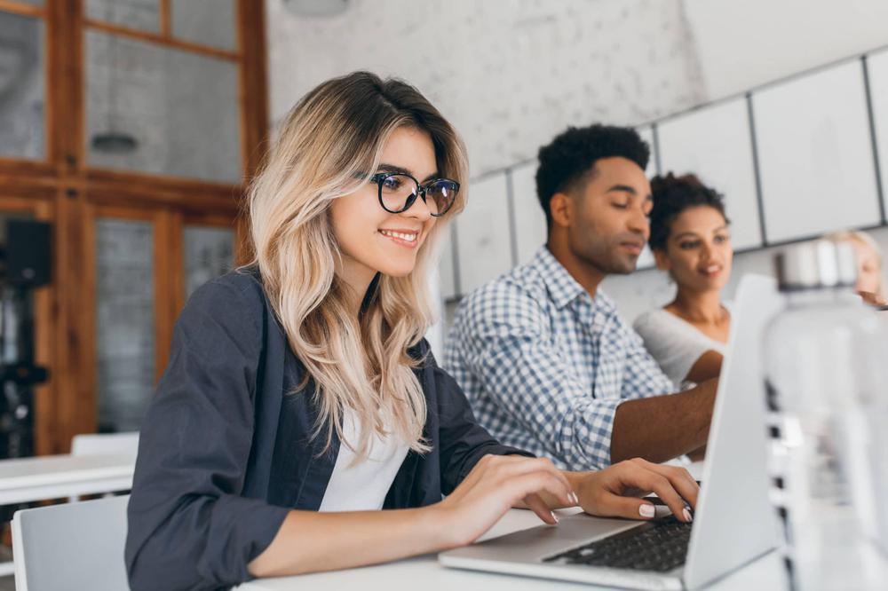 beautiful-curly-female-freelancer-with-cute-manicure-using-laptop-smiling-indoor-portrait-blonde-secretary-sitting-beside-african-coworker-blue-shirt-scaled